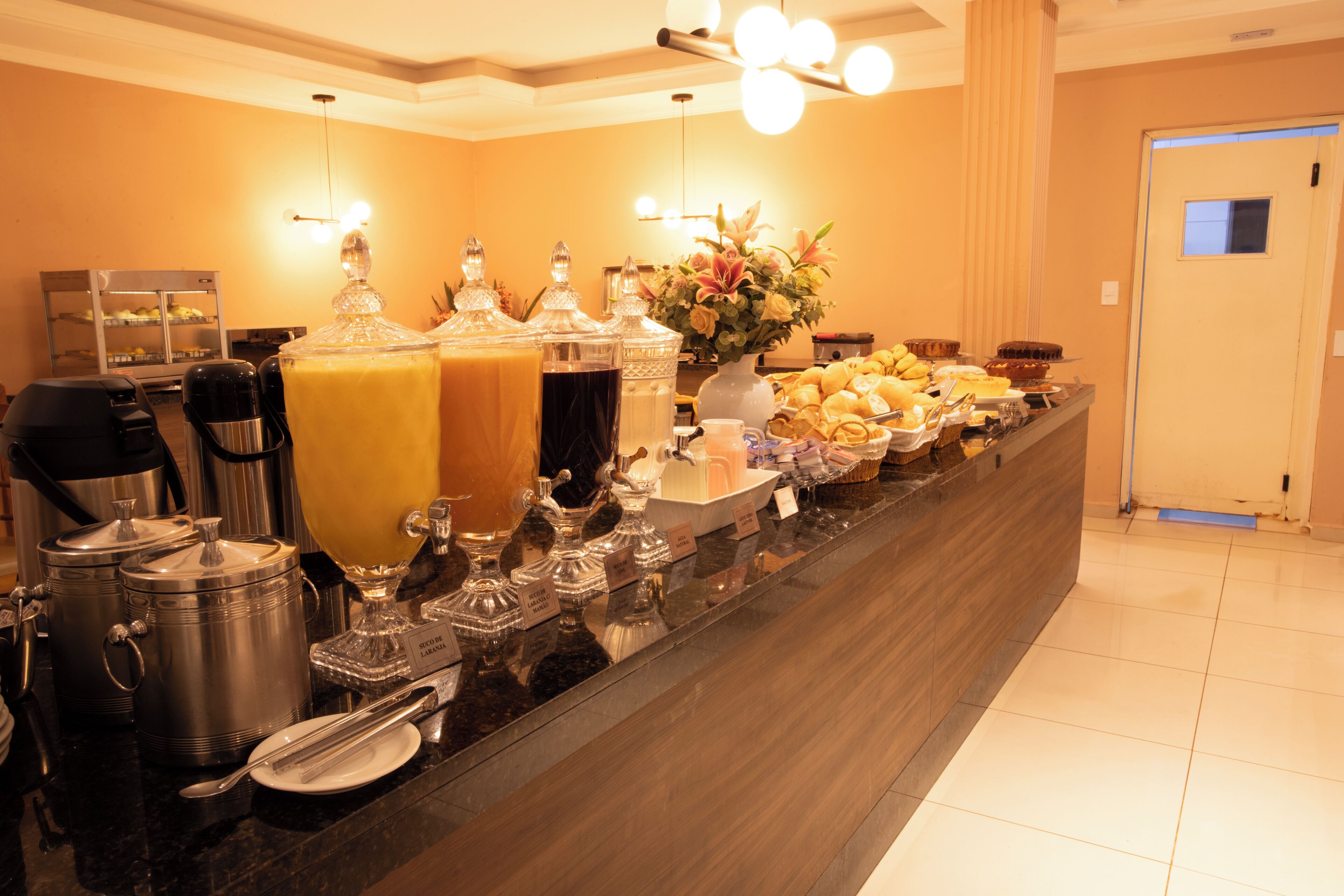 A buffet with various food items and beverages, a coffee machine, and a decorative vase.
