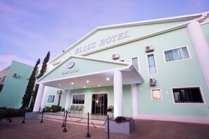 A hotel entrance with a sign reading 'ELLUS HOTEL,' a covered entrance, and a series of windows.