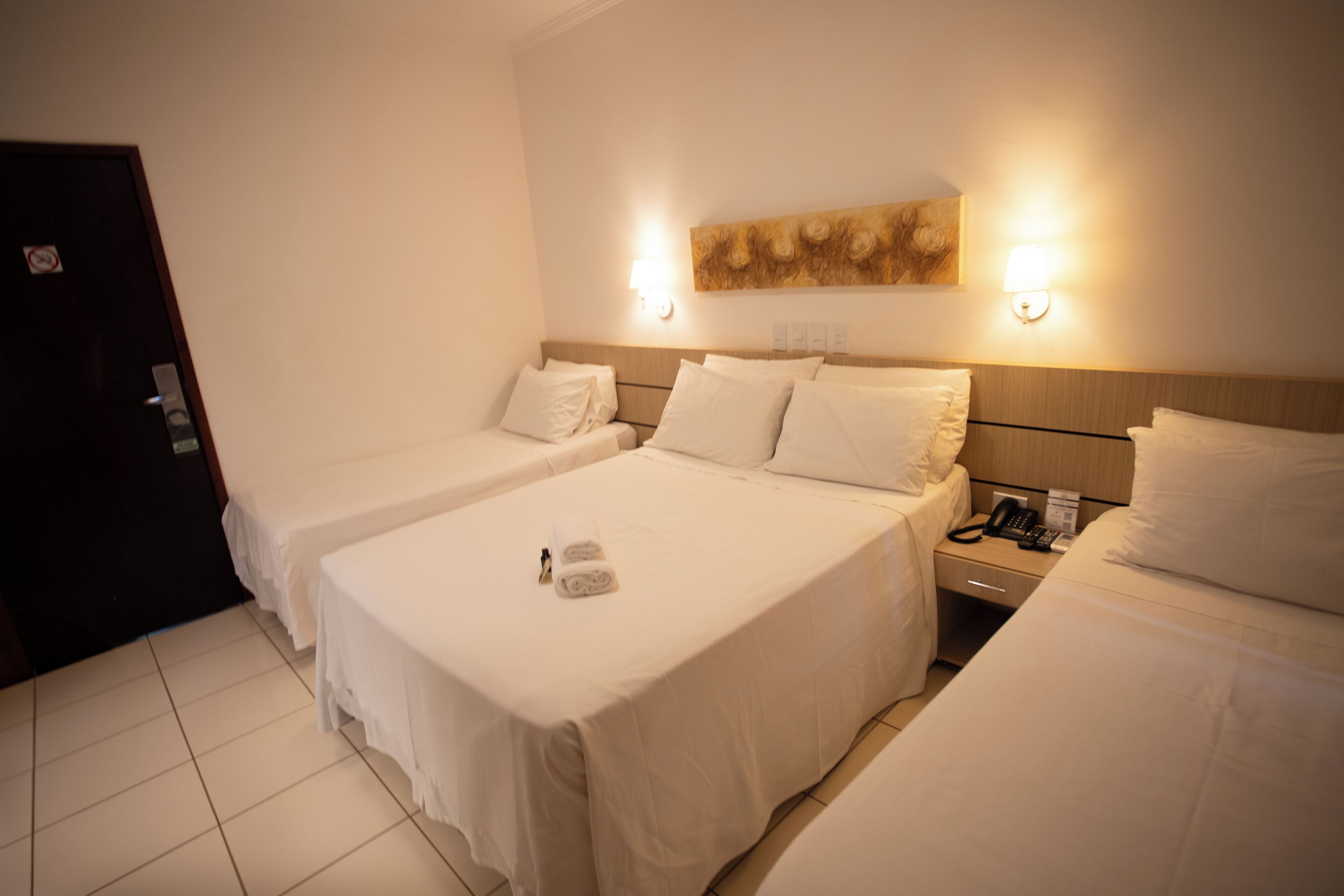 A hotel room with two beds, a wooden headboard, a painting on the wall, and a bedside telephone.