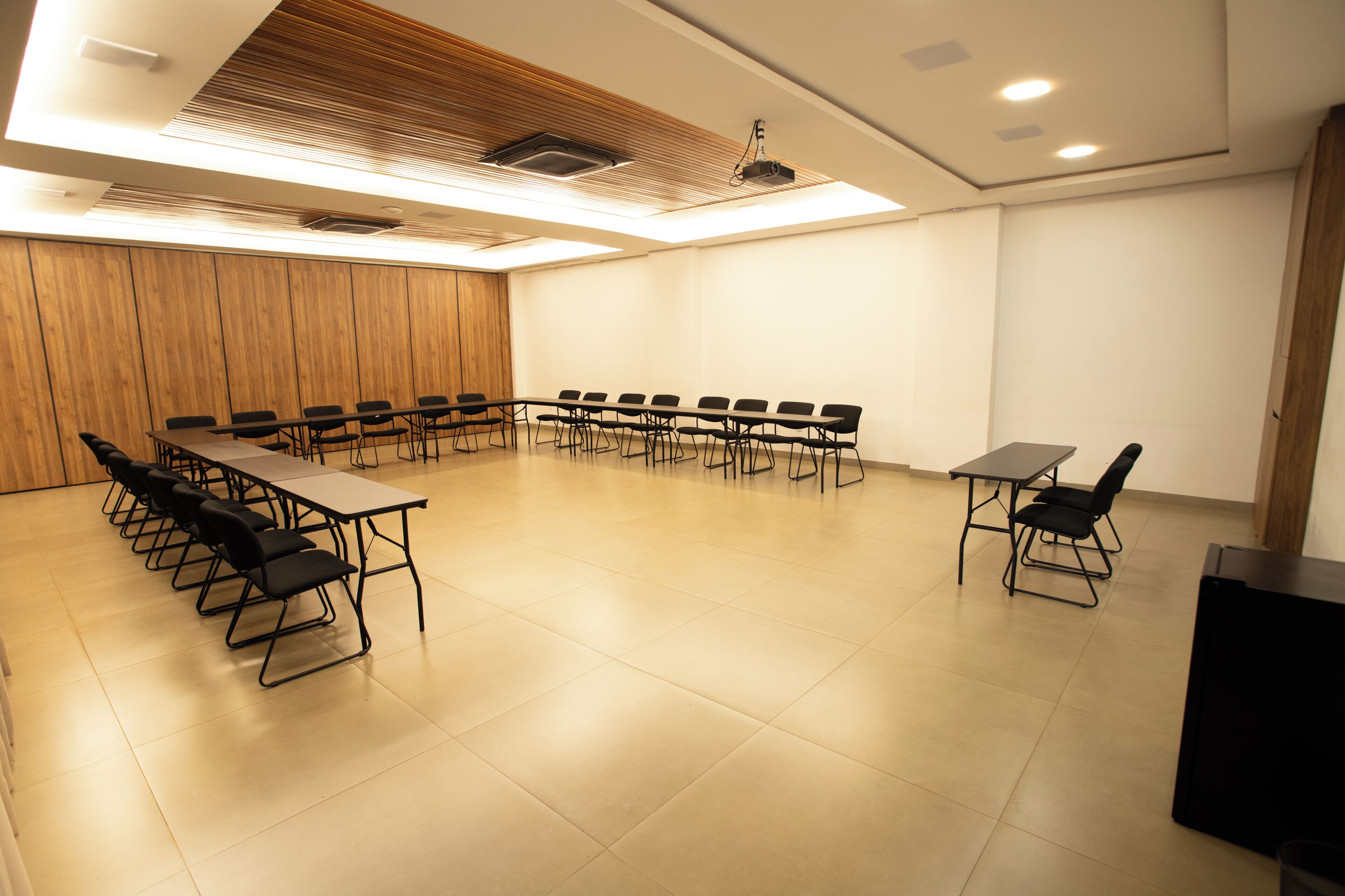 Una sala de conferencias con una larga mesa, sillas, un proyector y un panel de pared de madera.