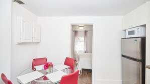 Une cuisine de taille réduite avec des meubles blancs, un réfrigérateur en acier inoxydable et une table à manger en verre, assortie de chaises rouges.