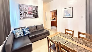 Ein modernes Wohnzimmer mit einer schwarzen Ledersofa, einem Esstisch mit gewobenen Platzsets und einem Stadtbild an der Wand.
