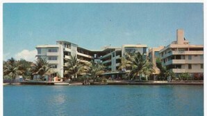 A coastal hotel with multiple floors, palm trees, and a body of water. - Beautiful Condo -Ocean View, Best Location, Pool, Parking & Steps to All U Want (San Juan)