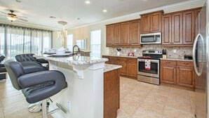 A modern kitchen with wooden cabinets, a central island, stainless steel appliances, and a dining area with black chairs. - Reunion 5 Bedroom Vacation Home 7824 (Kissimmee)