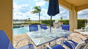 An outdoor patio with a glass table set for dining, surrounded by blue chairs, and overlooking a swimming pool. - Reunion 5 Bedroom Vacation Home 7824 (Kissimmee)