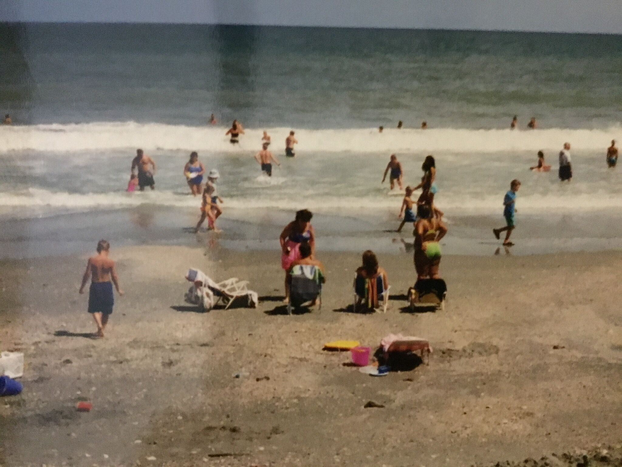 A beach with people walking and swimming.