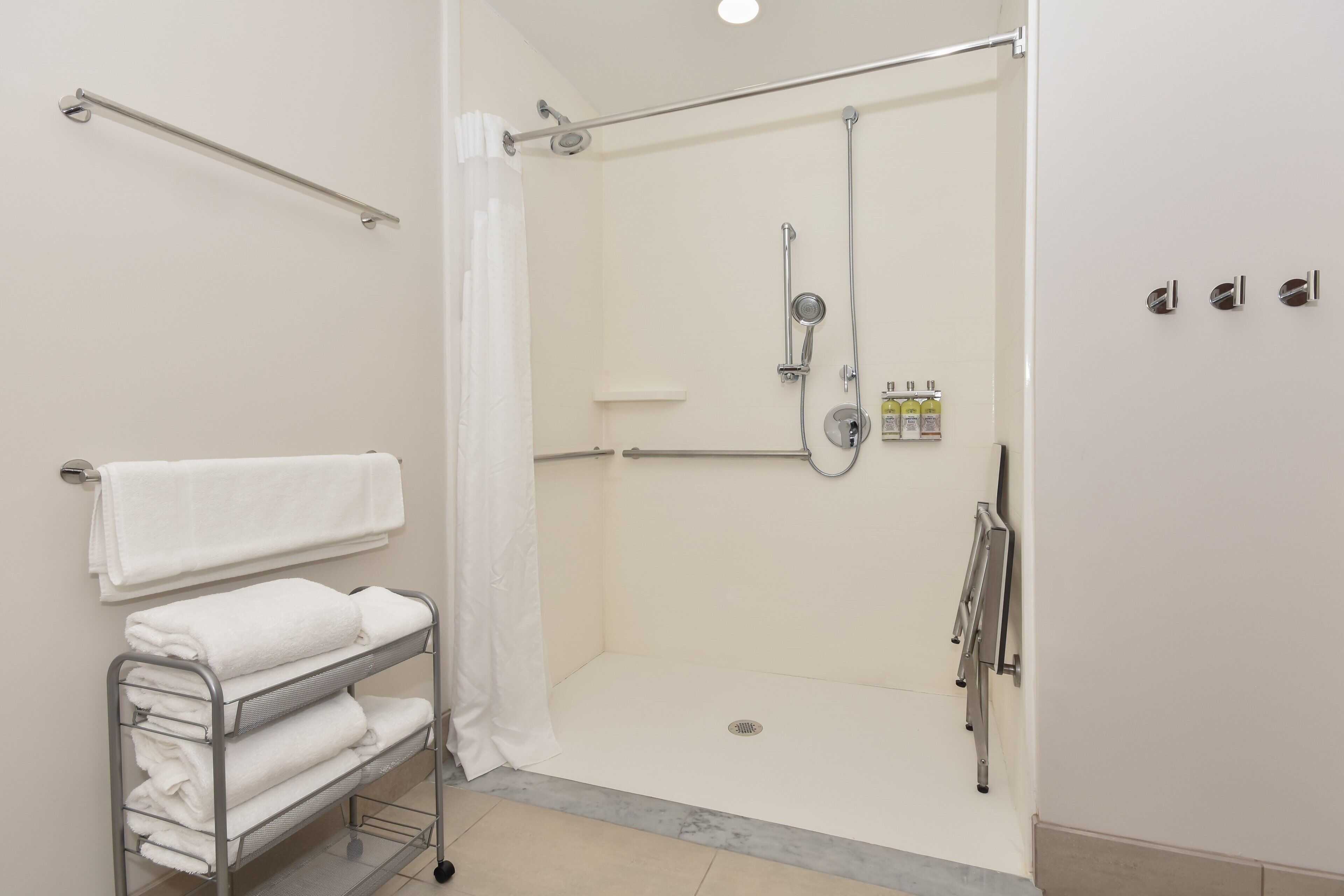 A modern bathroom with a walk-in shower, a towel rack, and a shelf with folded towels.