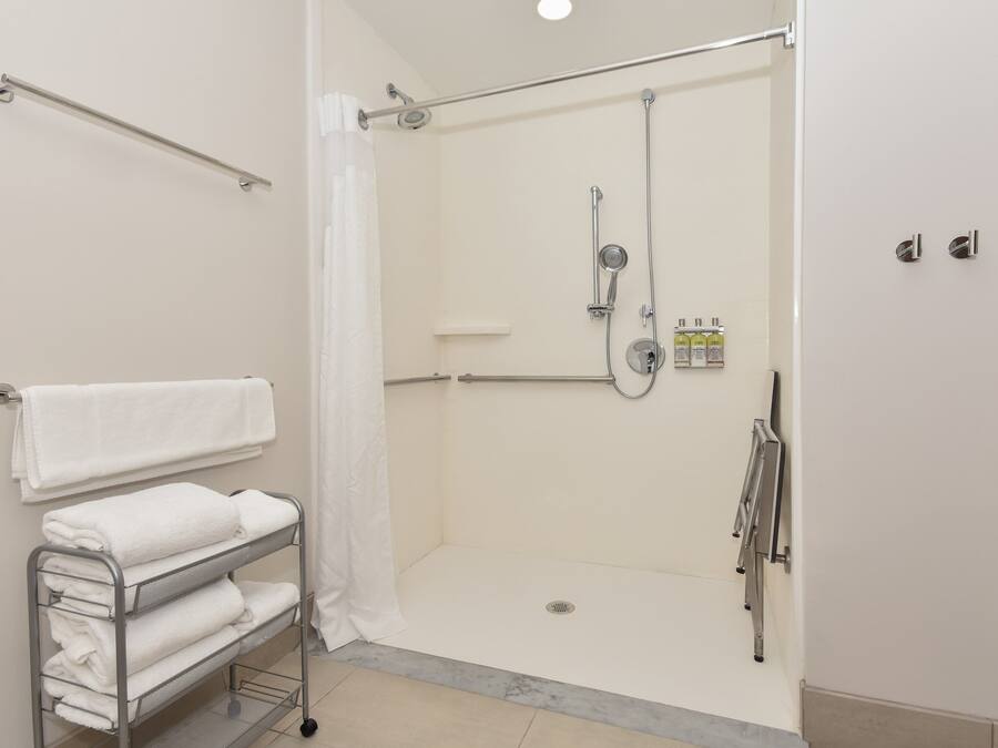 A modern bathroom with a walk-in shower, a towel rack, and a shelf with folded towels.