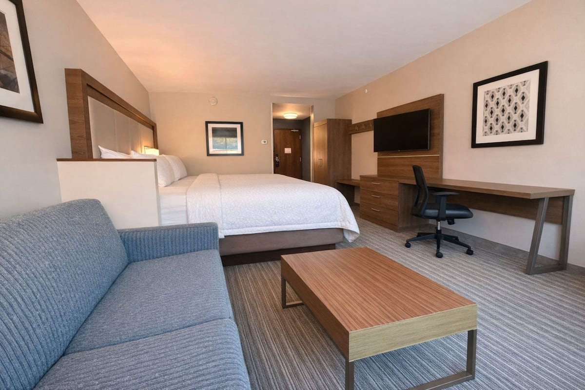 A hotel room with a bed, a sofa, a desk, a chair, and a TV.
