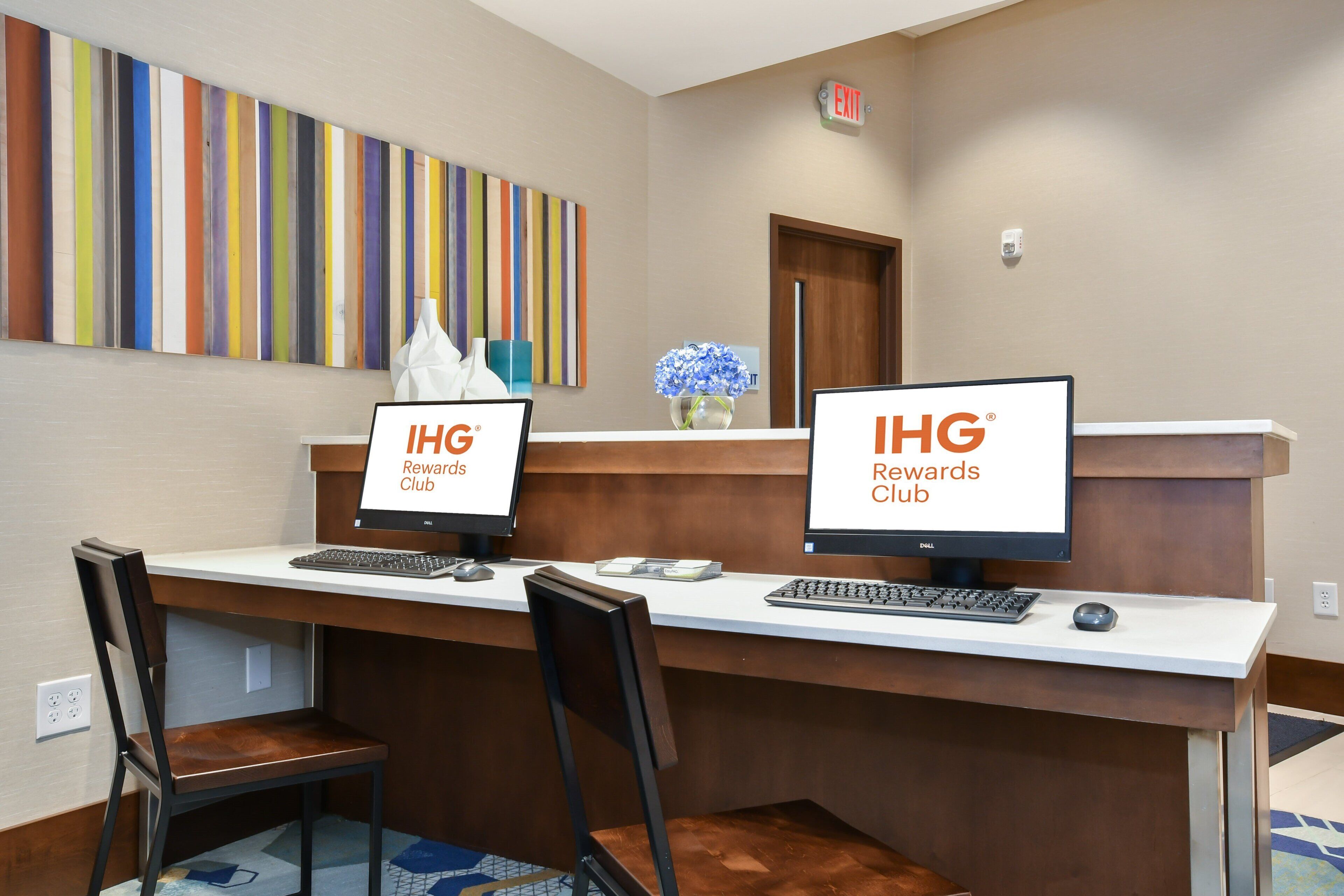 A reception desk with two monitors displaying 'IHG Rewards Club' and a colorful striped wall behind.