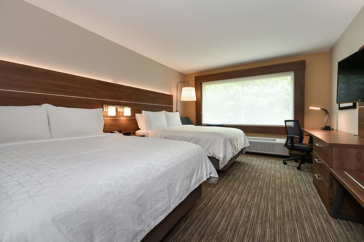 A hotel room with two beds, a desk, a chair, a TV, and a window with a view.