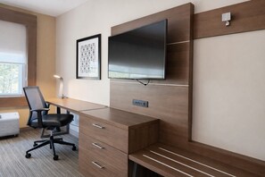 A modern office space with a wooden desk, a black office chair, a flat-screen TV mounted on the wall, and a framed picture above the desk.