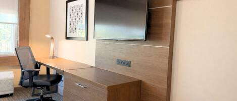 A modern office space with a wooden desk, a black office chair, a mounted flat-screen TV, and a framed picture on the wall.