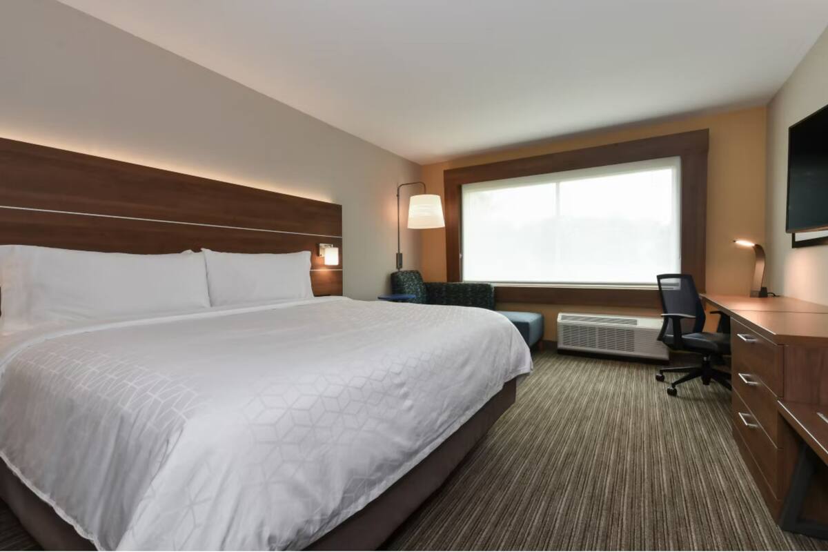 A hotel room with a large bed, a desk, a chair, a TV, and a window with blinds.