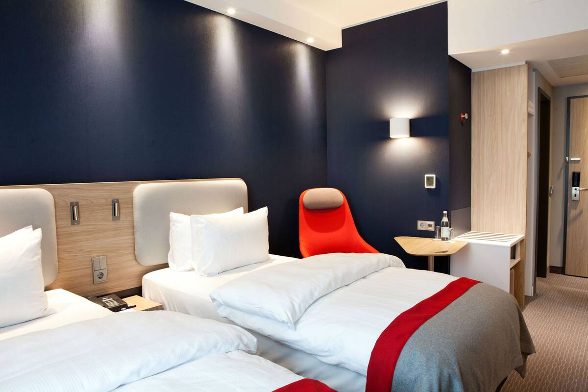 A hotel room with two beds, a red chair, a small table, and a nightstand.