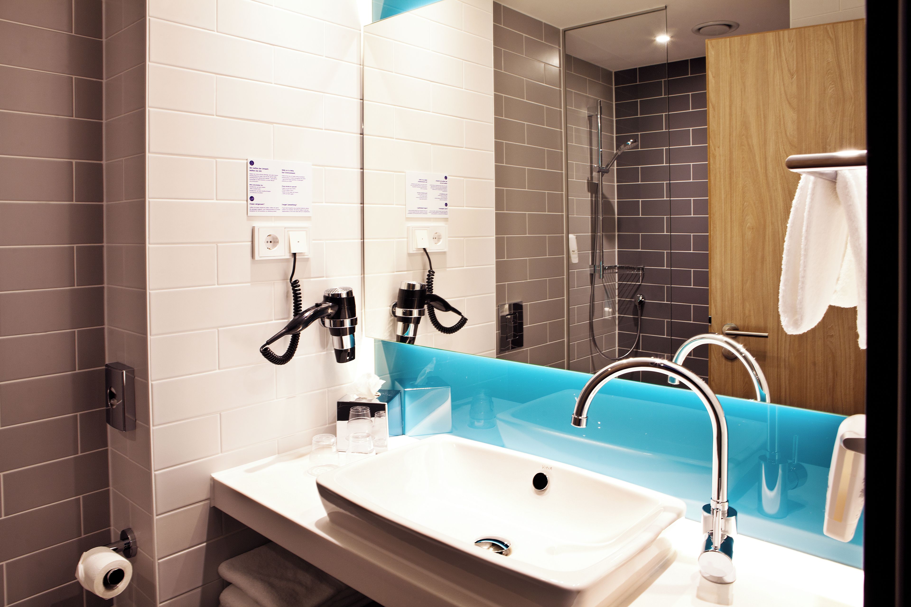A modern bathroom with a white sink, a mirror, and a shower area.
