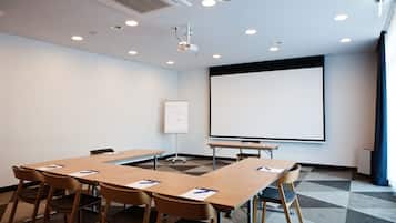 A conference room with a large table, chairs, a projector, a whiteboard, and a screen.