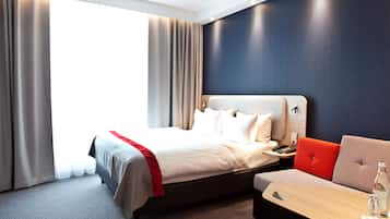Una habitación de hotel moderna con una cama grande, un sofá, una mesita y vistas al exterior.