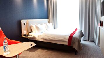 A hotel room with a bed, a desk, a chair, a water bottle, and a TV.