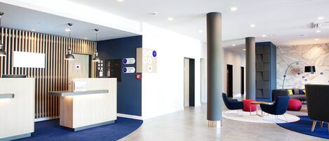 Un área de recepción moderna con un mostrador de madera, una alfombra azul y una zona de estar con sillas coloridas y un mapa en la pared.