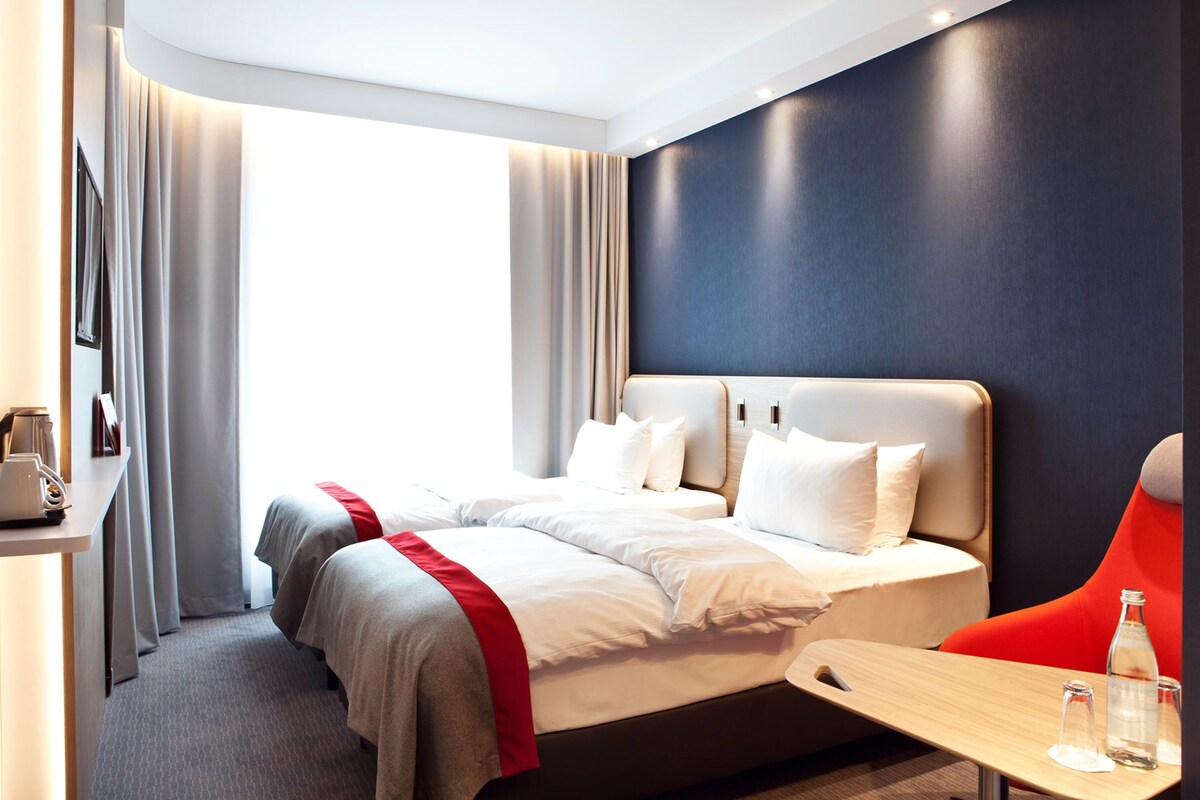 A modern hotel room with a large bed, a desk, and a chair.