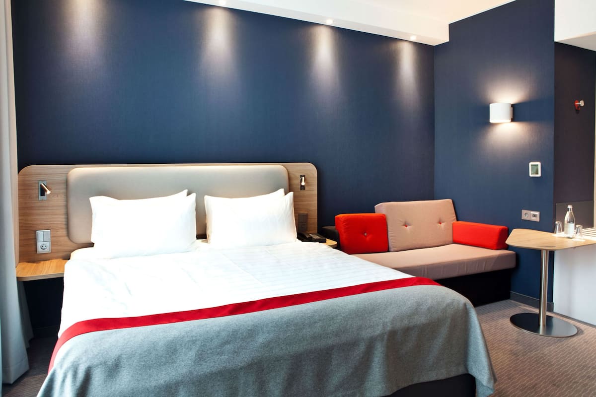 A modern hotel room with a large bed, a sofa, and a small table.