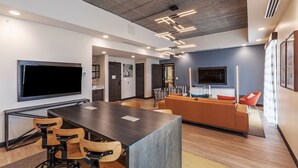 Um interior moderno com uma mesa de jantar comprida, banquetas de bar, um sofá e uma televisão de tela plana na parede.