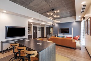 A modern interior with a long dining table, bar stools, a sofa, and a flat-screen TV mounted on the wall. - Hotel Indigo Tulsa DWTN-Entertainment Area by IHG (Tulsa)