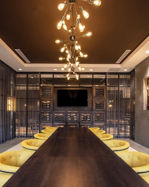 Un interior moderno con una larga mesa de madera oscura, sillas tapizadas en amarillo, un televisor de pantalla plana grande y un candelabro único.