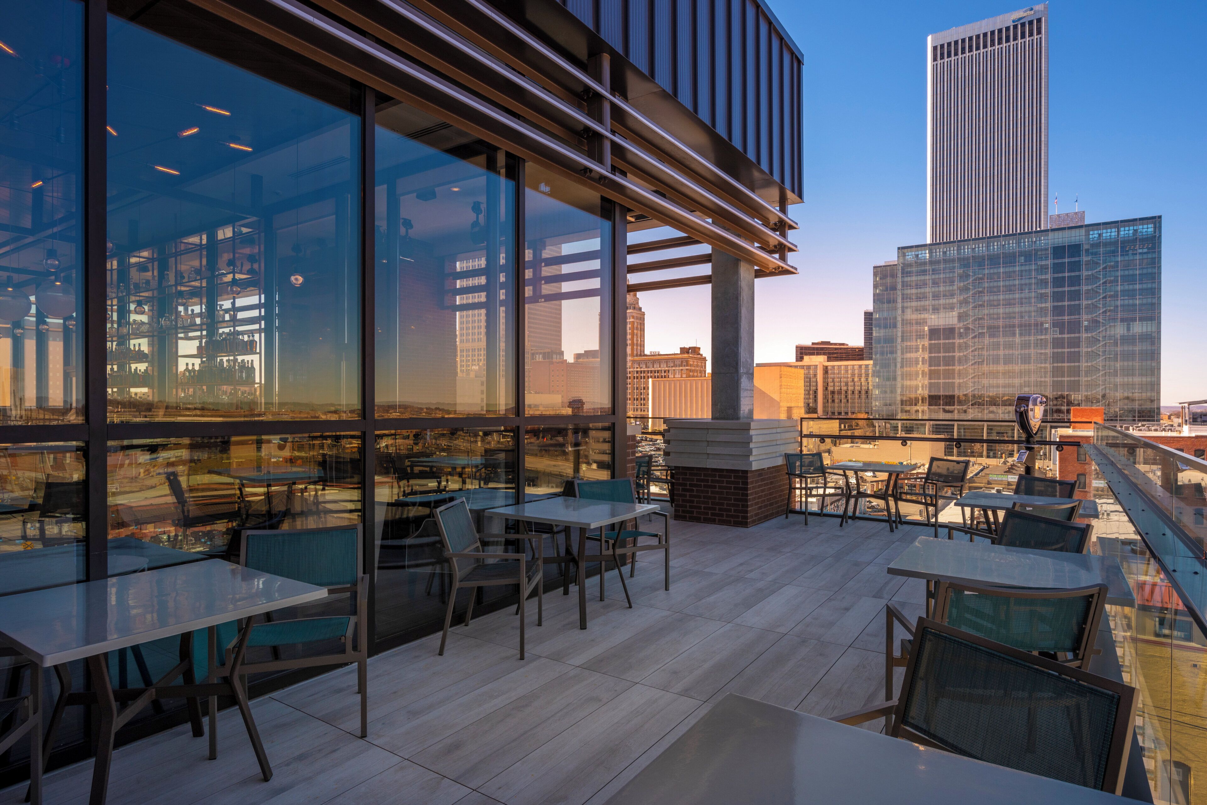 Un espace extérieur aménagé avec des tables et des chaises, de grandes fenêtres et une vue sur les toits de la ville.