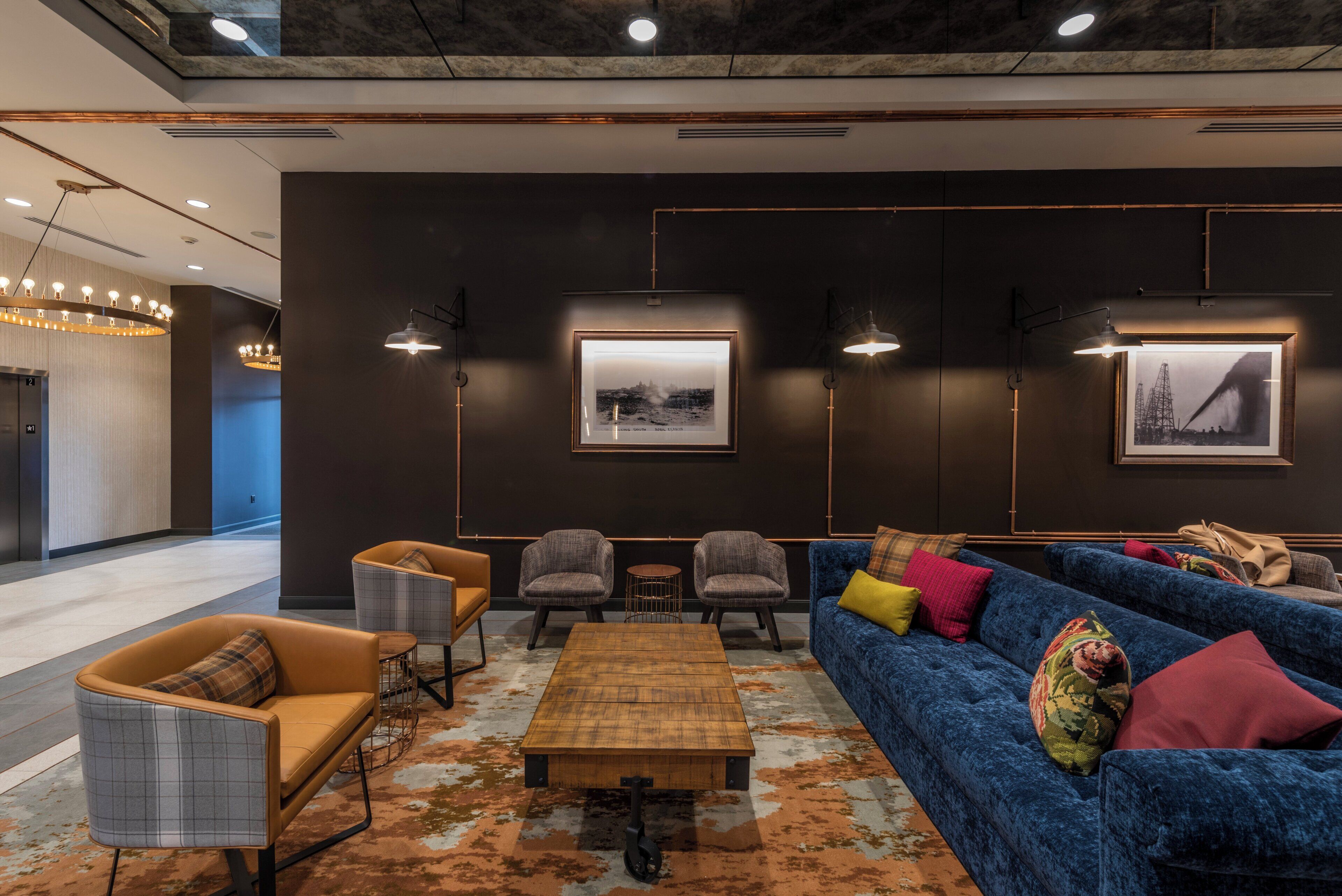A modern lounge area with a blue sofa, armchairs, a coffee table, and framed pictures on the wall.