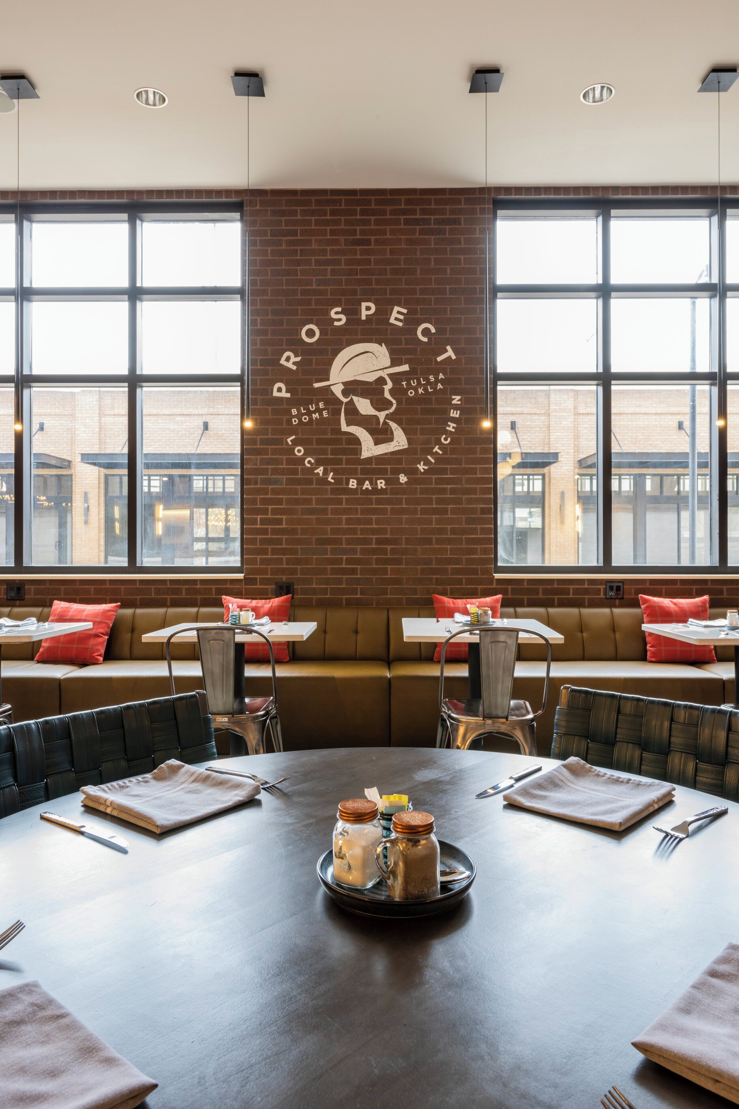 A restaurant interior with a brick wall, large windows, and a central table with a dessert display.