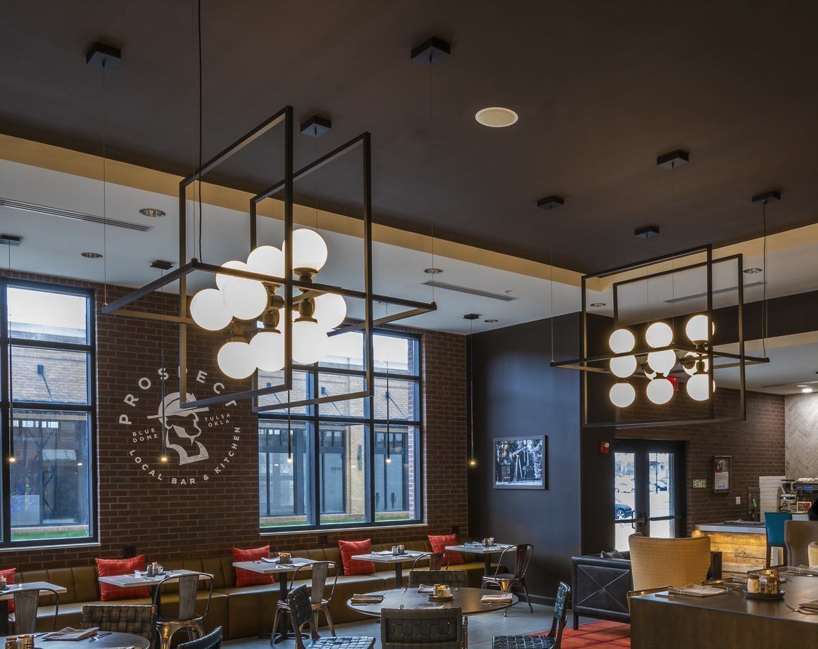 A modern restaurant interior with high ceilings, exposed brick walls, and large windows.