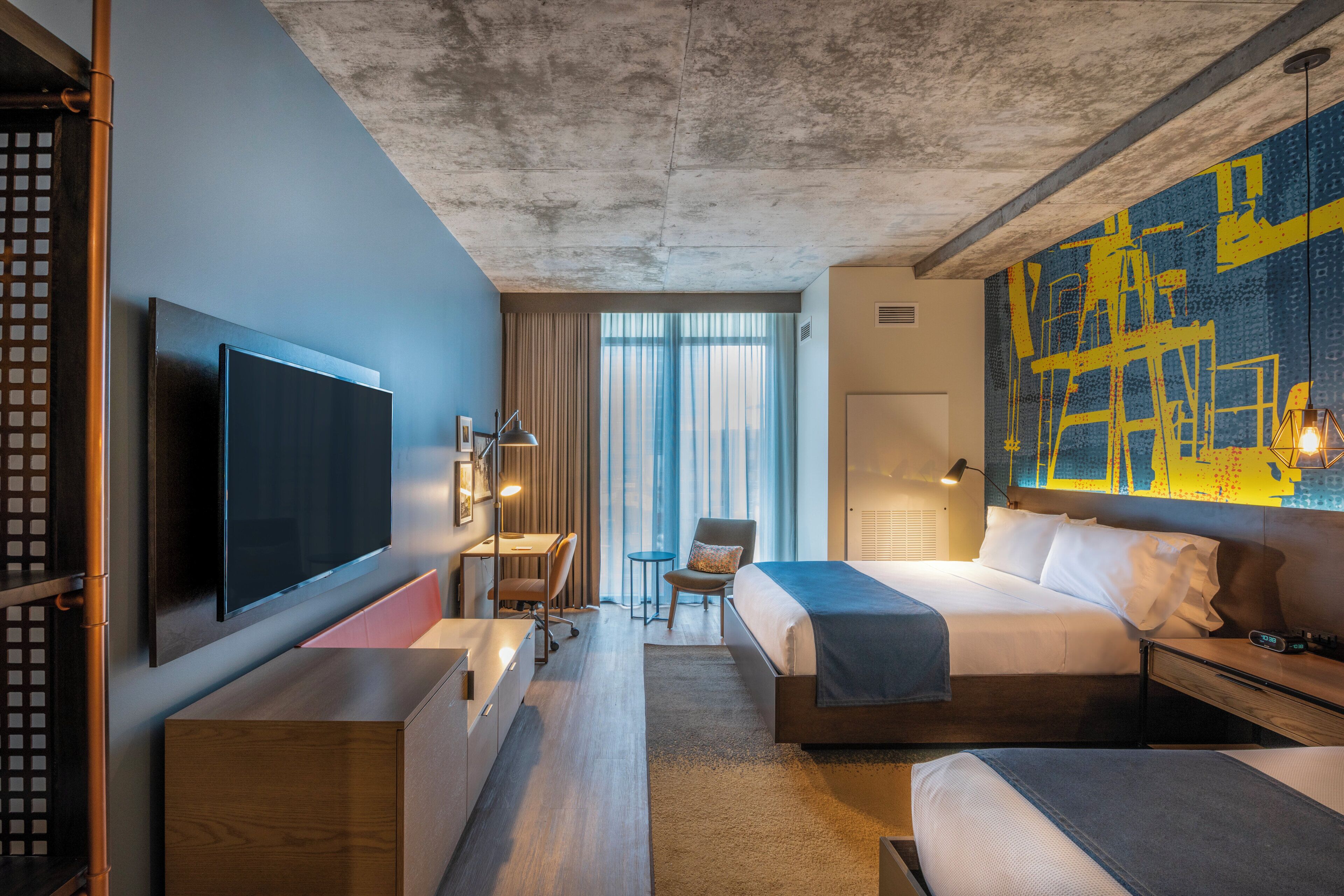 Ein Hotelzimmer mit einem großen Bett, einem Schreibtisch, einem Flachbildfernseher und Blick auf die Stadt durch das Fenster.