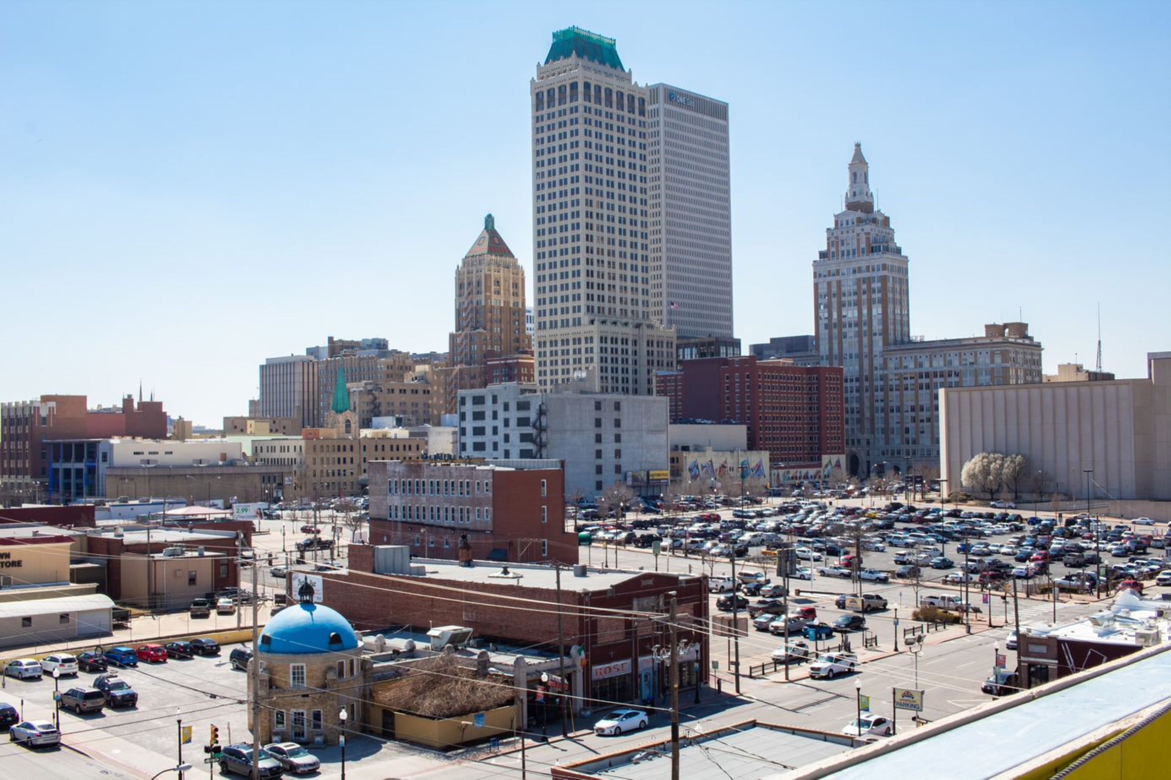 A cityscape with a parking lot filled with cars, various buildings, and a prominent blue-domed structure.