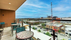 Een balkon met een tafel en stoelen, met uitzicht op een stadsgezicht met gebouwen en een hoge zendmast.