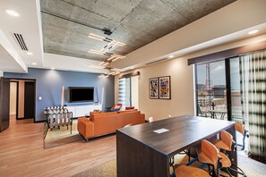A modern office space with a large meeting table, orange sofas, and a TV on the wall. - Hotel Indigo Tulsa DWTN-Entertainment Area by IHG (Tulsa)