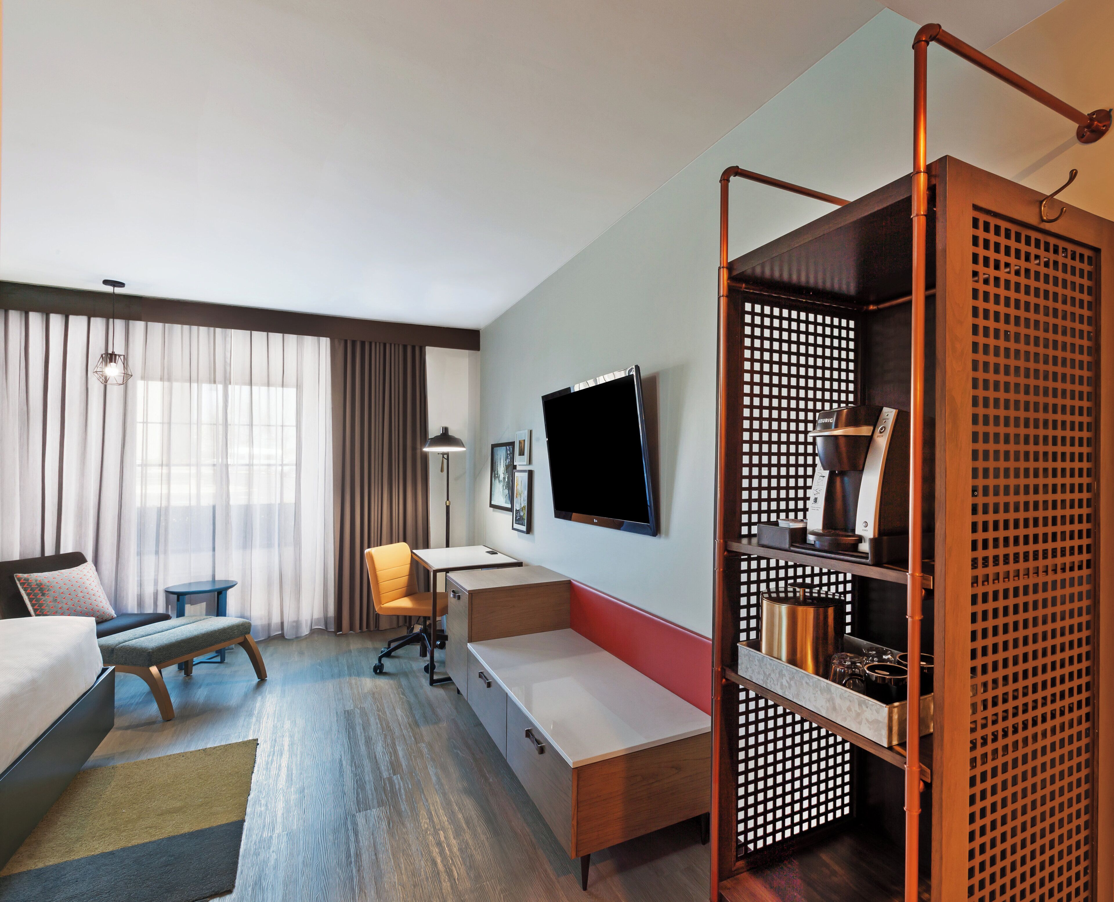 A hotel room with a bed, a desk, a chair, a TV, and a coffee machine.