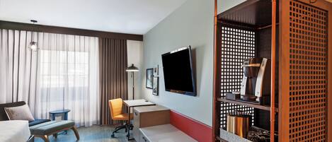 A hotel room with a bed, a desk, a chair, a TV, and a coffee machine.