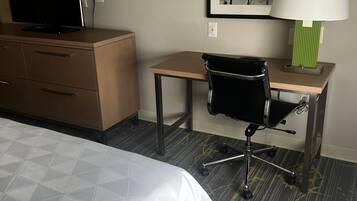 A hotel room with a bed, a desk, a chair, a television, a lamp, and a framed picture on the wall.