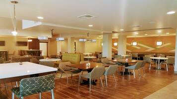 Une salle à manger d’hôtel avec plusieurs tables et chaises, un éclairage au plafond et un motif décoratif sur le mur.