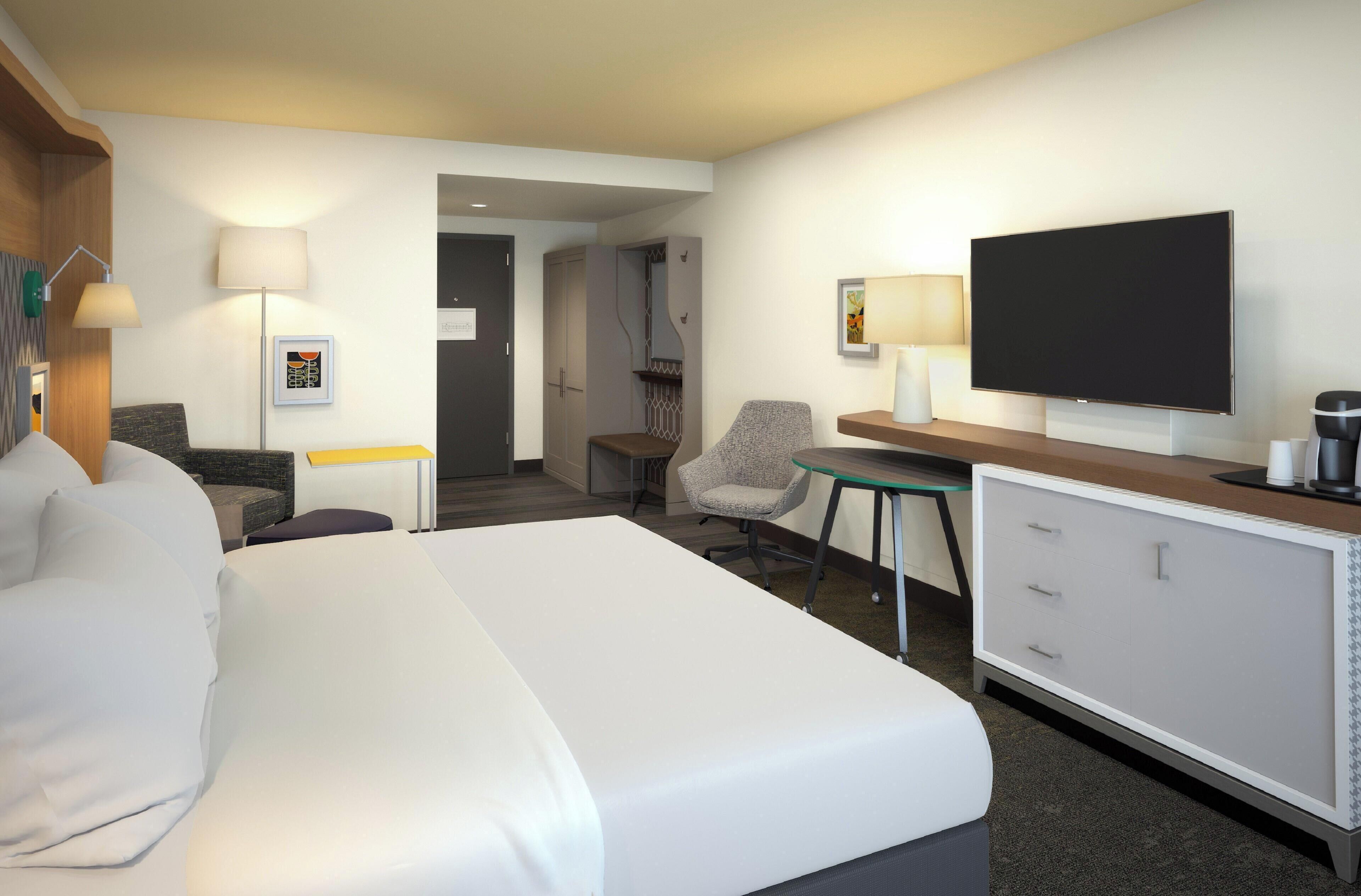 A hotel room with a bed, desk, chair, television, and a small table with a lamp.