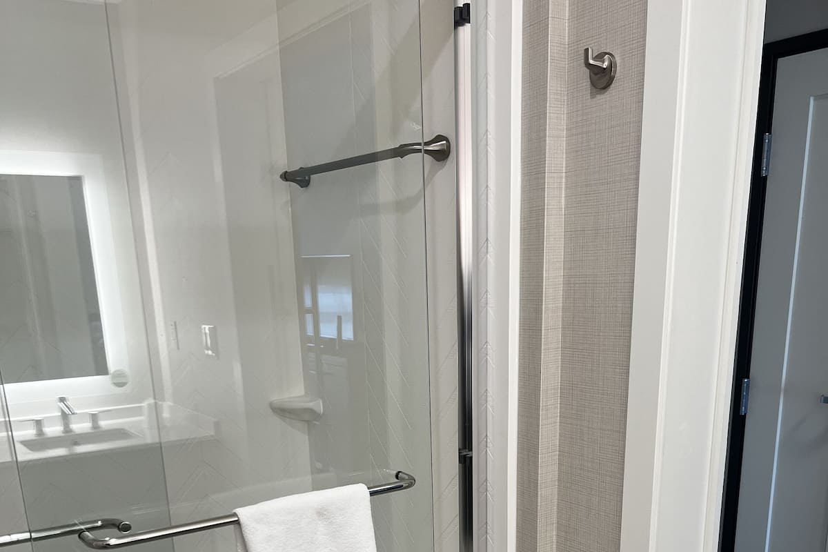 A modern bathroom with a glass-enclosed shower, a white towel hanging on the door, and a visible sink area.