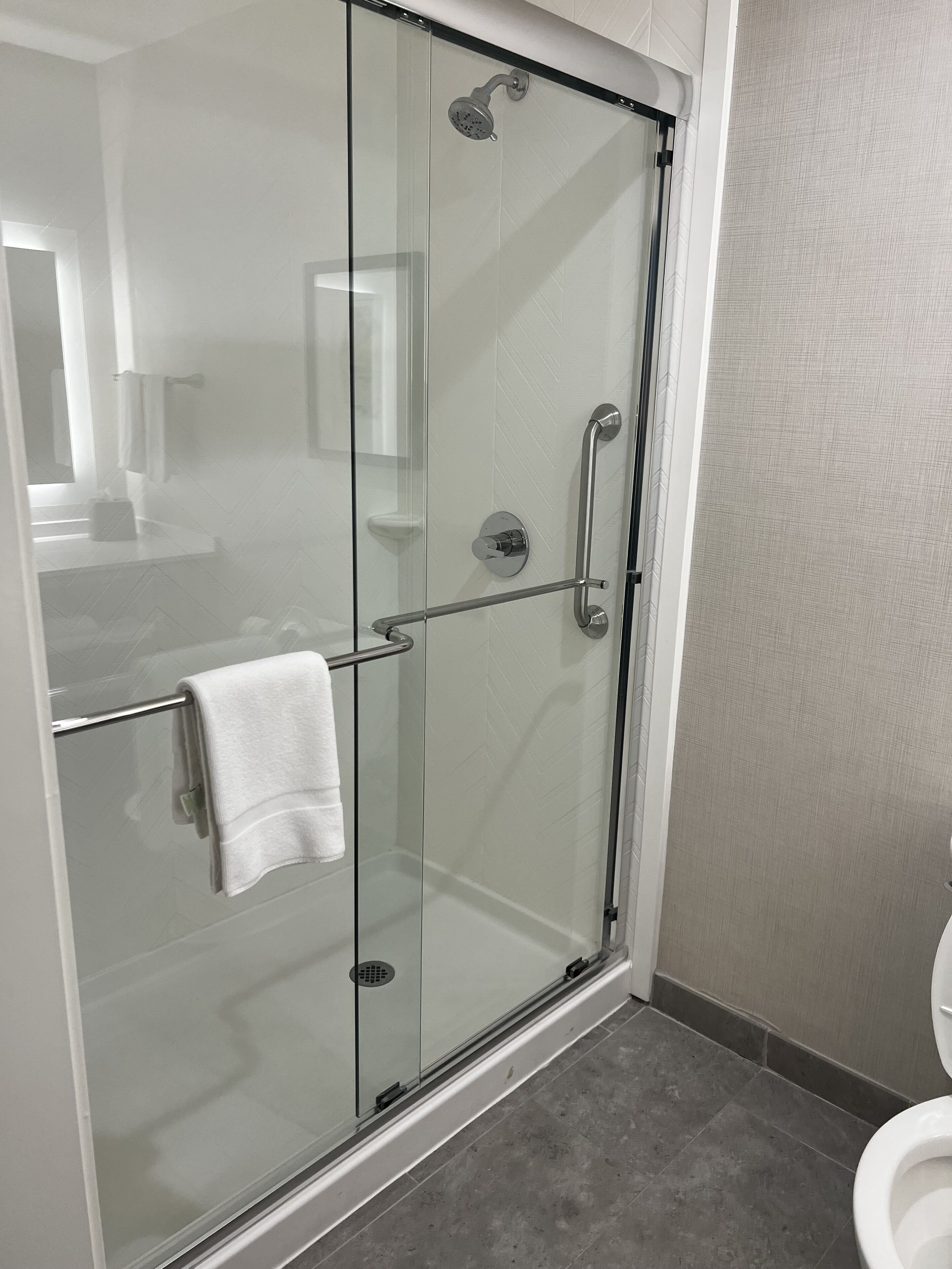 A glass-enclosed shower with a white towel on the door handle, a glass shower door, and a tiled floor.