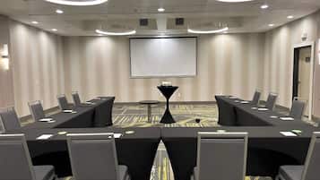 Une salle de conférence équipée d’une longue table, de chaises, d’un écran de projection et d’une petite table avec une lampe.