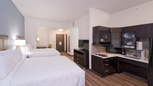 Une chambre d’hôtel avec deux lits, un bureau, une télévision, un four à micro-ondes et une petite kitchenette.