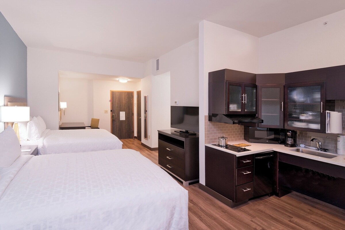 Een hotelkamer met twee bedden, een bureau, een televisie, een magnetron en een kleine kitchenette.