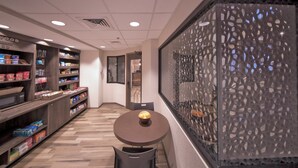 A modern interior with a wooden counter displaying snacks, a round table with a bowl, and a decorative wall with a geometric pattern.