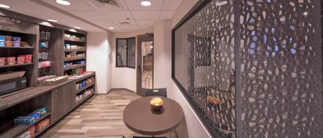 A modern interior with a wooden counter displaying snacks, a round table with a bowl, and a decorative wall with a geometric pattern.
