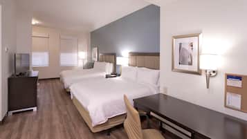 Habitación de hotel con dos camas, un escritorio, una silla, un televisor y un tablón de anuncios.